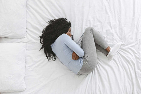 Woman on bed curled up cramping
