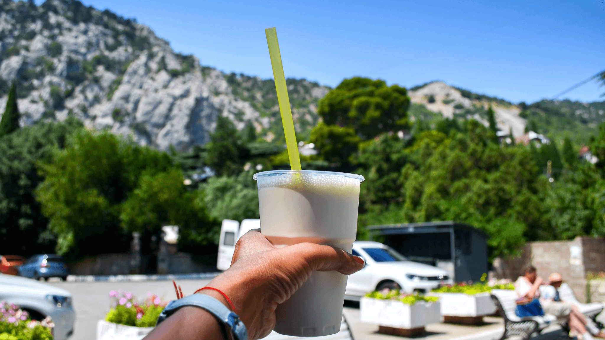  Arm of a woman carries in her hand a glass of almased drink with a background of mountains with snow