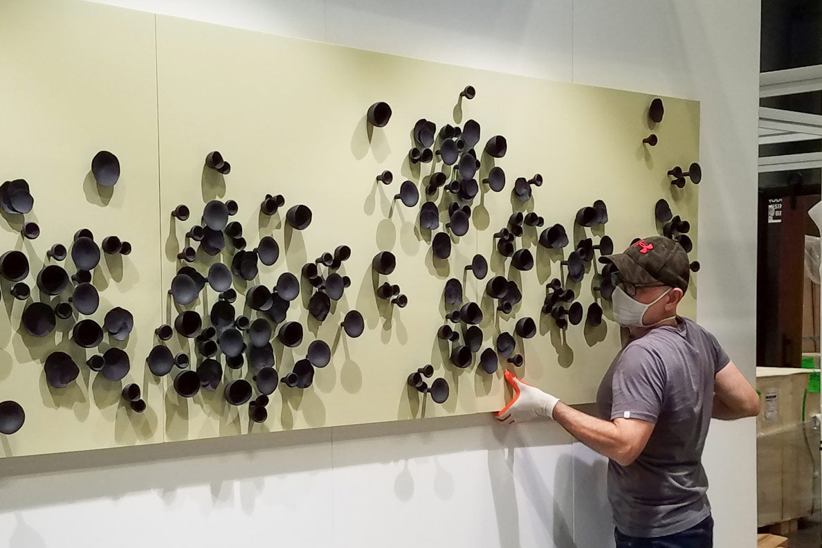 Mam mounting black Wall Play™ sculptural art to a white wall at the Gold Leaf Design Group booth at BDNY.