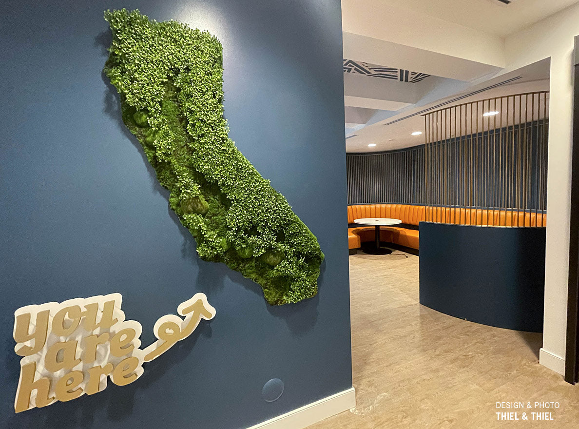 A green wall shaped like California with a large room beyond. A words sculpture saying "you are here" points towards Green Wall.