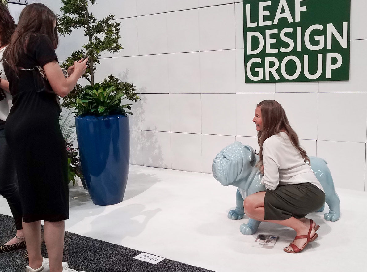 Person posing with a blue bulldog sculpture at a Gold Leaf Design Group tradeshow display.