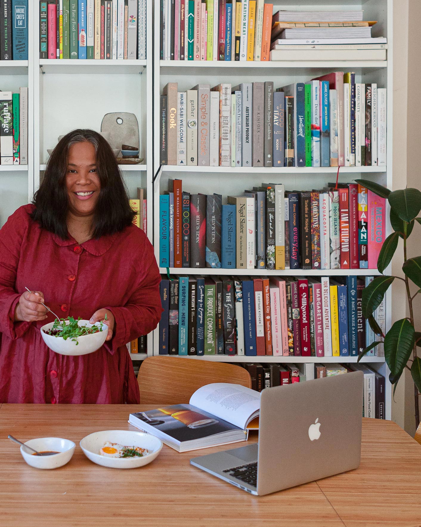 Luisa standing in front of her huge collection of cookbooks, holding a winterwares bowl