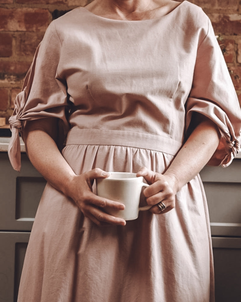 Holding a Winterwares cup, wearing a pink linen dress
