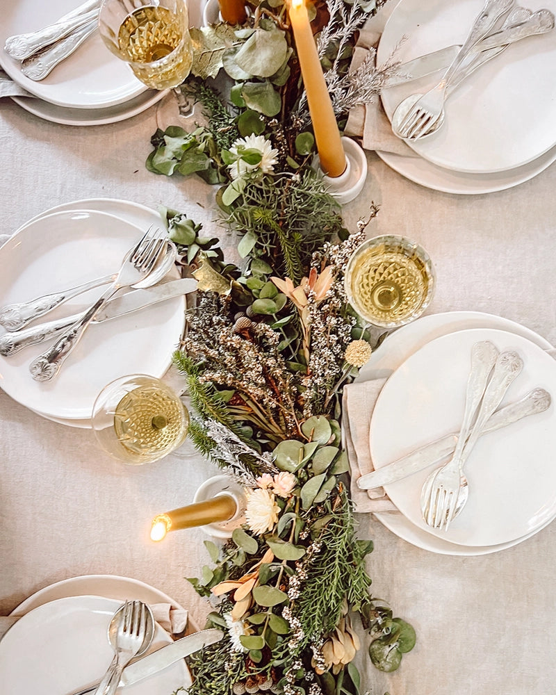 A close-up of a Christmas table garland made from native foliage, with lit candles adding a warm glow.