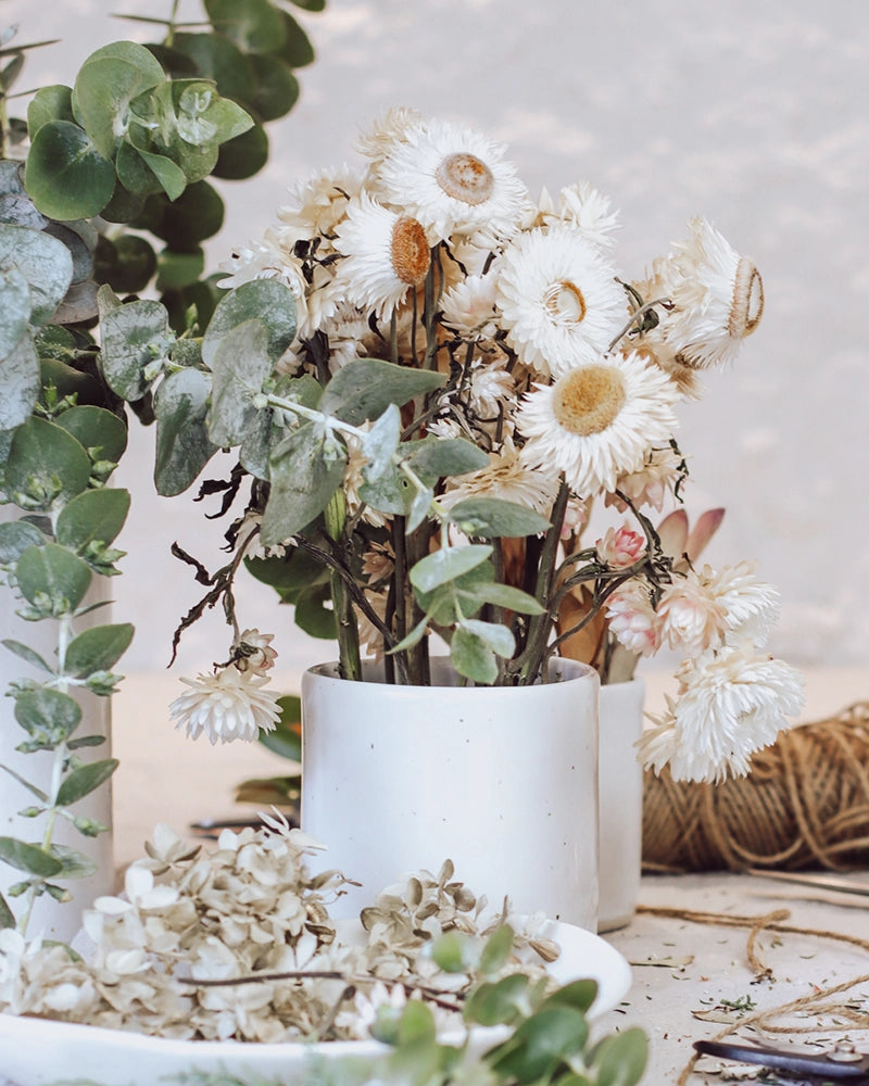 A rustic white ceramic vase filled with dried white flowers and greenery, part of a Christmas table décor