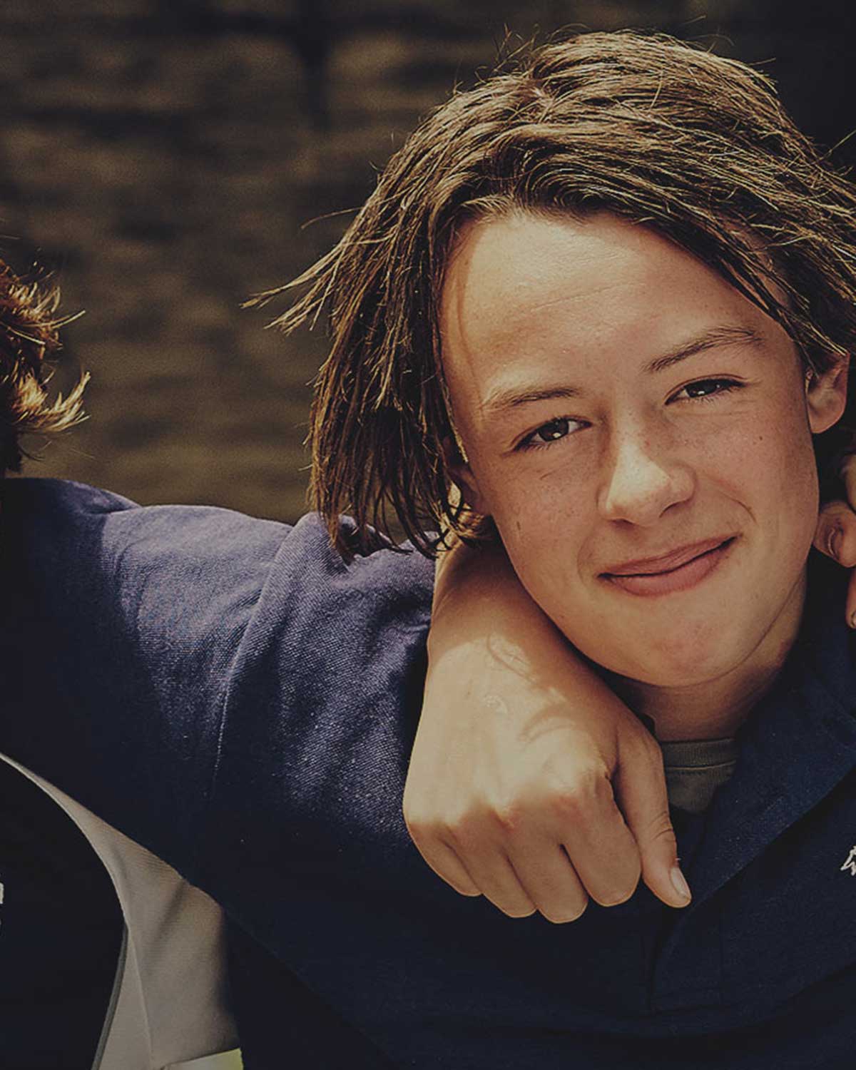 A school aged boy facing the camera and smiling, with his arm around a friend