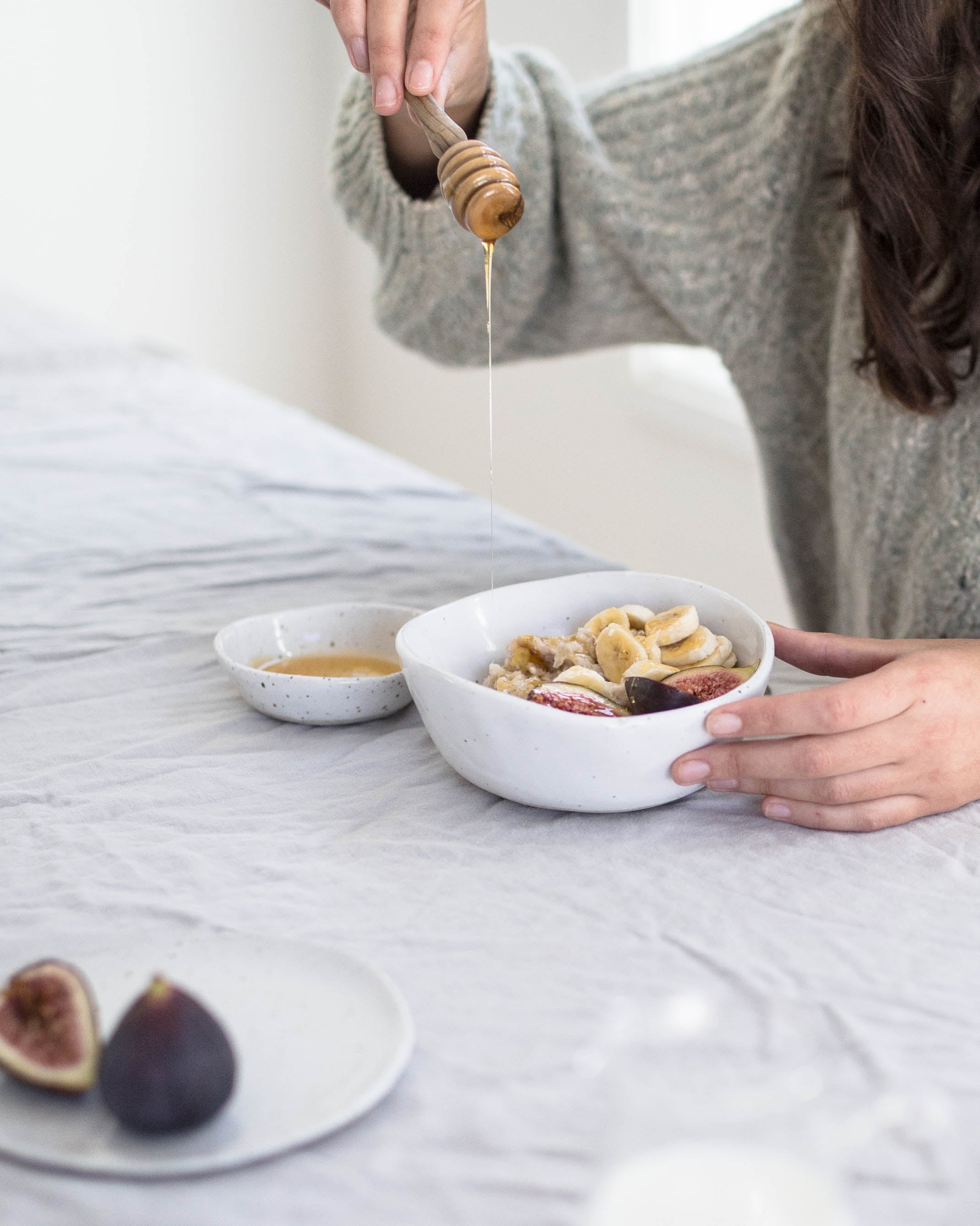 Pouring honey over a bowl of hot porridge. Having breakfast from handmade ceramics makes everyday special.