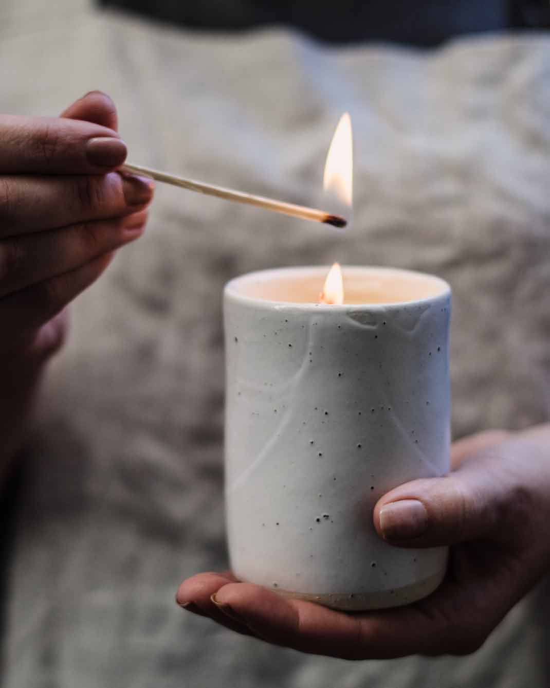 Hand cradling Winterwares Woodland Trail candle whilst being lit with match