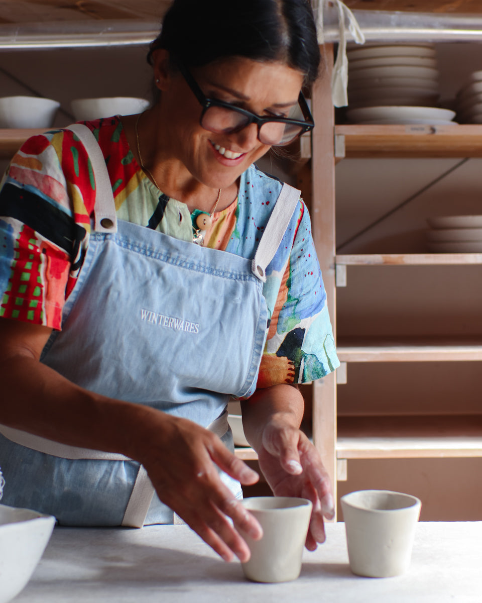 Woman placing newly made clay cups on a bench in a pottery studio