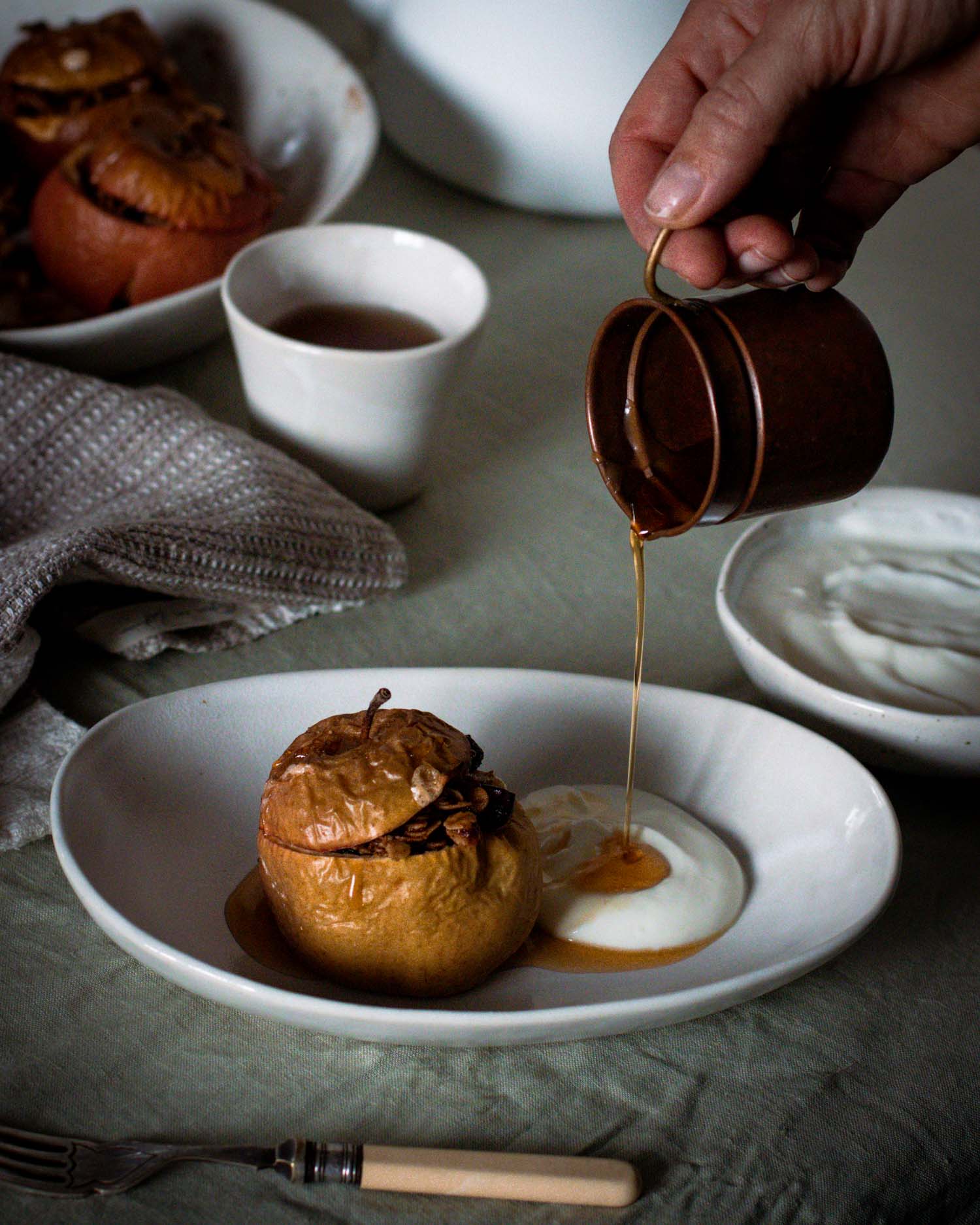 Pouring maple syrup over baked apples in a handmade ceramic bowl