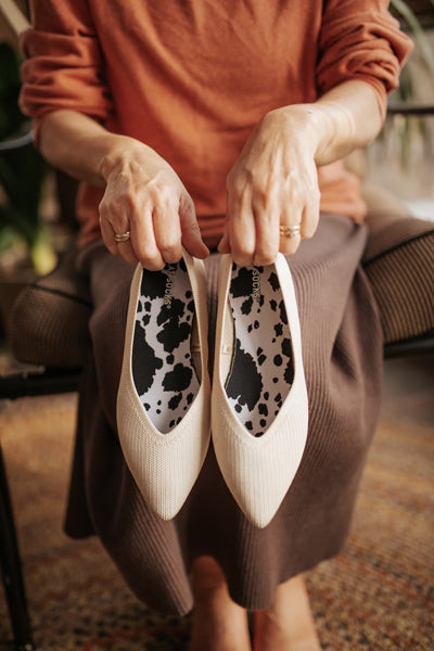 woman holding beige flats with cow print sock liners inside