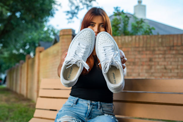 woman sitting on bench holding white shoes with tan FLAT SOCKS inside