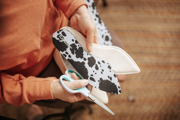 woman holding scissors while trimming cow print sock insert