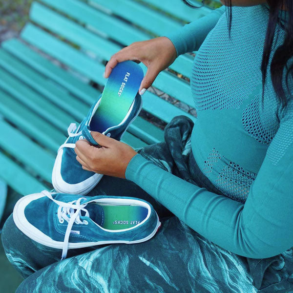 Woman placing blue green ombre FLAT SOCKS inside blue sneakers