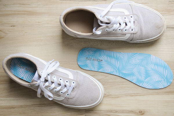 gray tennis shoes with blue FLAT SOCKS shoe inserts on wood floor