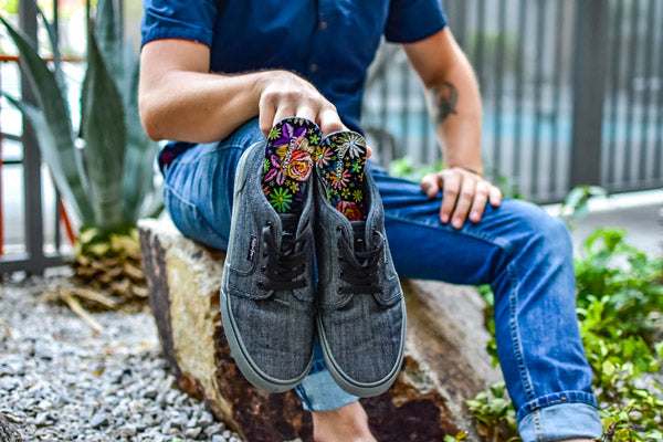 man sitting on a rock and holding gray slip on shoes with floral sock insoles inside