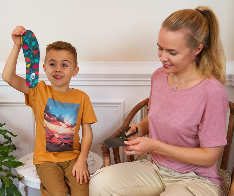 Boy holding FLAT SOCKS Kids while mother trims barefoot shoe insert