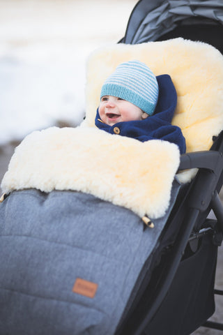 Kind sitz in einem Kinderwagen mit Wintersack. Das Kind strahlt vor Glück