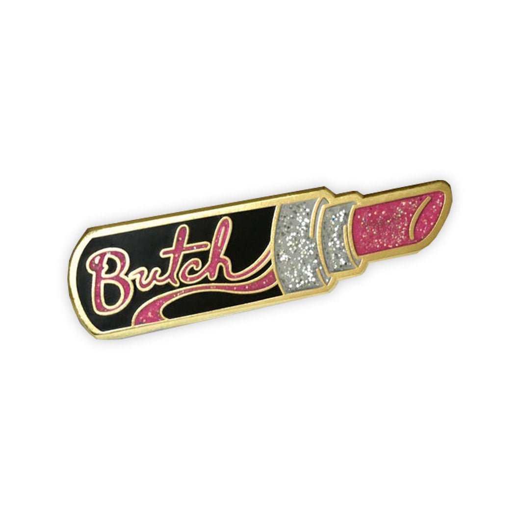A gold enamel pin of a open black tube of pink glittery lipstick with 
