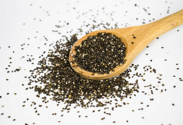 chia seeds spilling out of a wooden spoon onto a white background