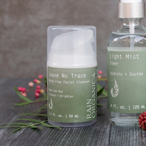 dead sea mud cream cleanser in an airless bottle on a gray wood with textured background and pink pepper tree sprig