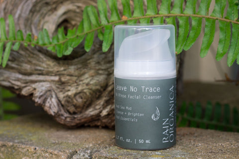 Rain Organica's Leave No Trace Rinse Free Facial Cleanser on a moss covered brick wall with driftwood and ferns behind