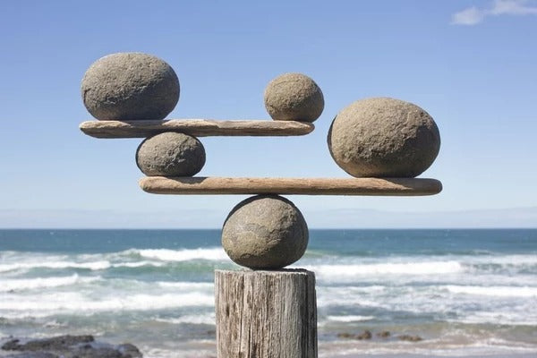 rocks perfectly balanced atop each other on rock seesaws next to ocean blue sky in background