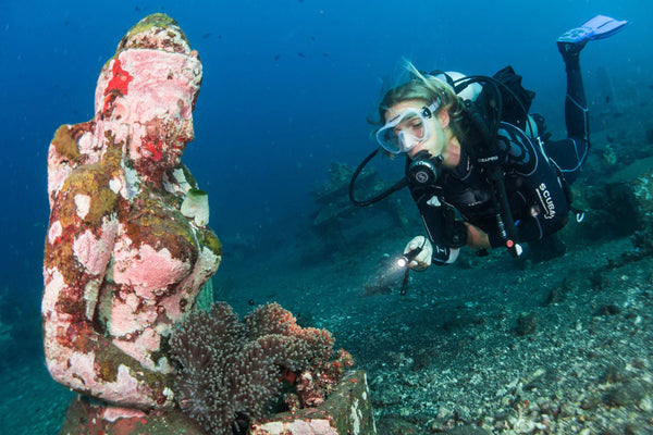 woman diver looking at underwater statue of a woman with a bed of sea anemones growing in her lap