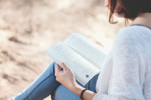 woman reading a book under a tree outside with natural light cascading around