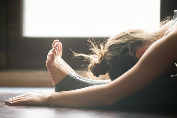 woman practicing yoga sitting on mat in forward fold