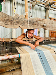 artisan smiling and standing behind handloom weaving a blanket