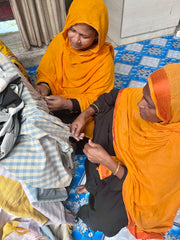 2 women in orange sari platting tassels on handloom blankets