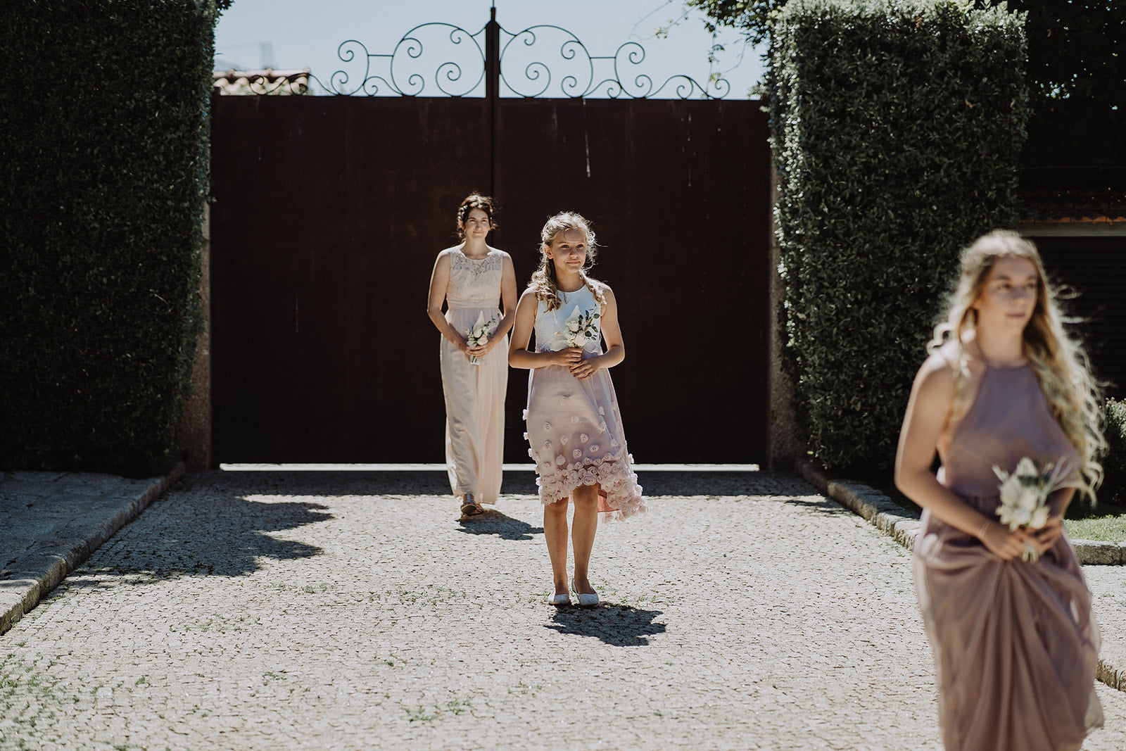 The Bridesmaids walking down the isle, in the garden setting, holding flowers.