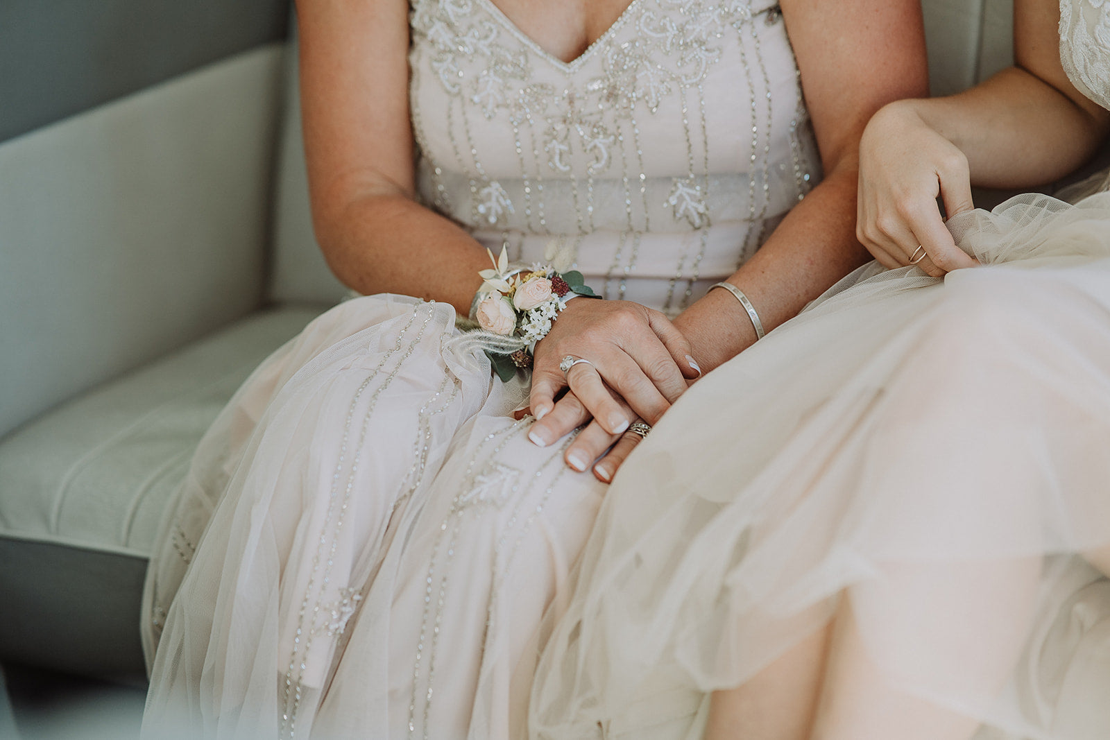 Eco-friendly wedding corsage, worn on the wrist. Close up of two women, seated, wearing bridal and mother of the bride dresses in neutral colours.