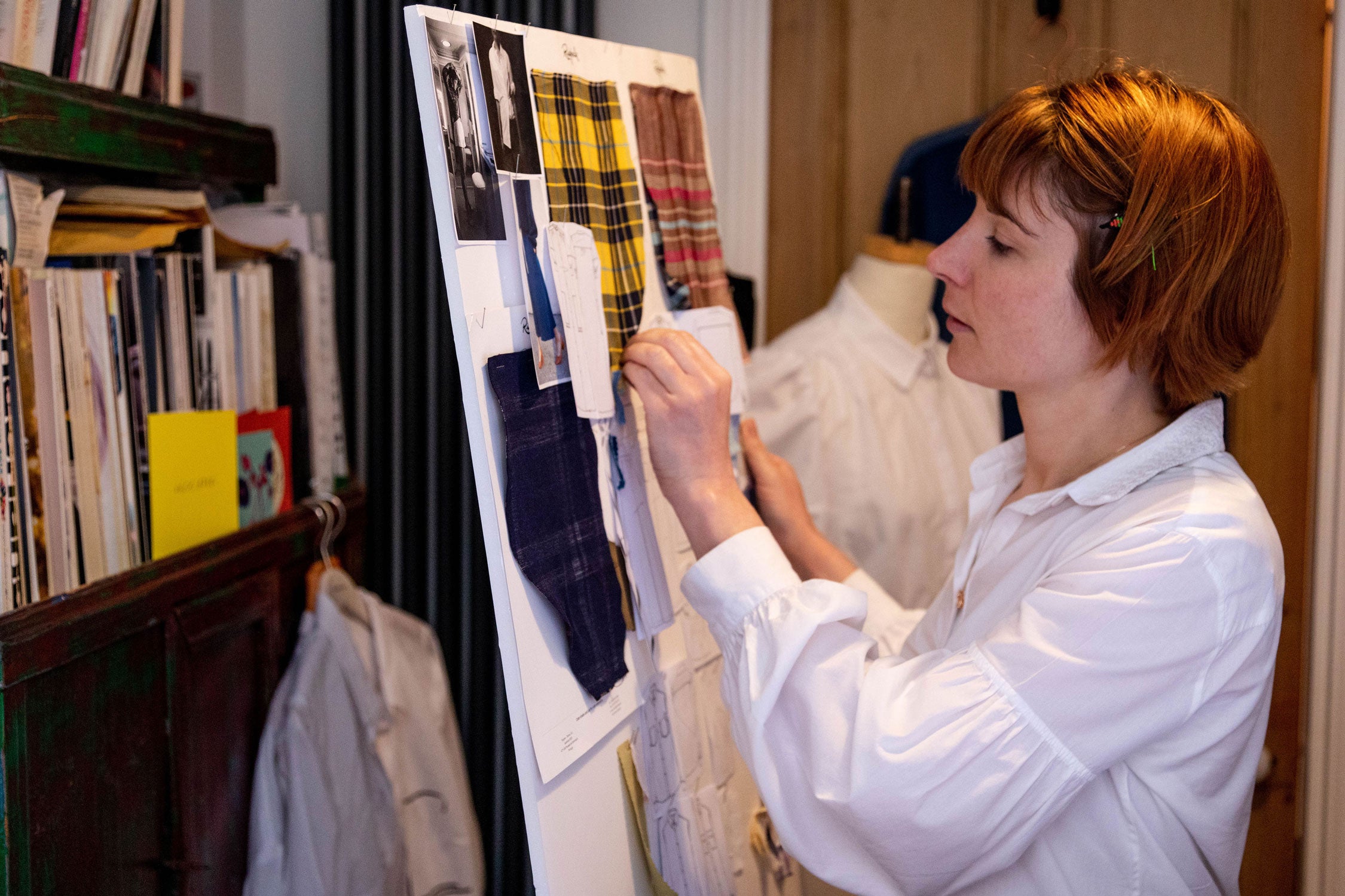 Saywood founder, Harriet, reviewing the fabrics and collection on a board in the London studio. Various fabric can be seen, with vintage magazines on a shelf in the background.