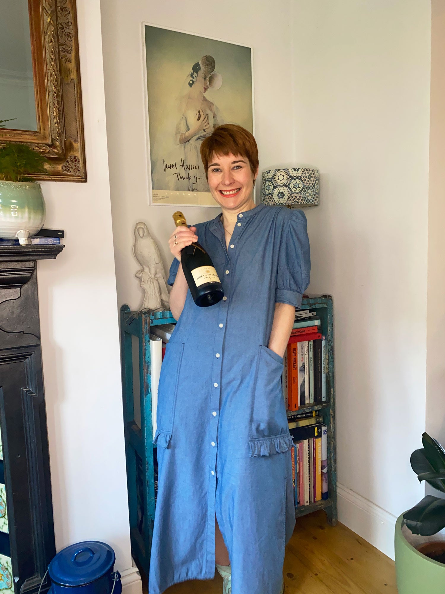 Saywood founder Harriet, holding a bottle of champagne in celebration of the Positive Luxury Award. She is wearing the Rosa Puff Sleeve Dress in lightwash Japanese Denim