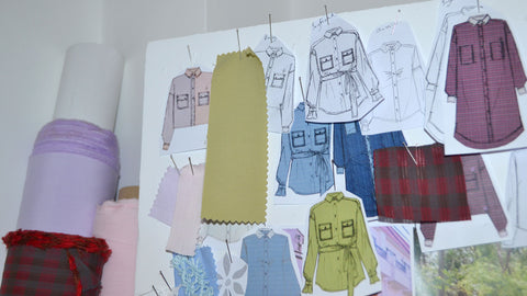 Saywood sketches pinned to a board with fabrics for the design process. The top of fabric rolls can be seen to the left of the image.