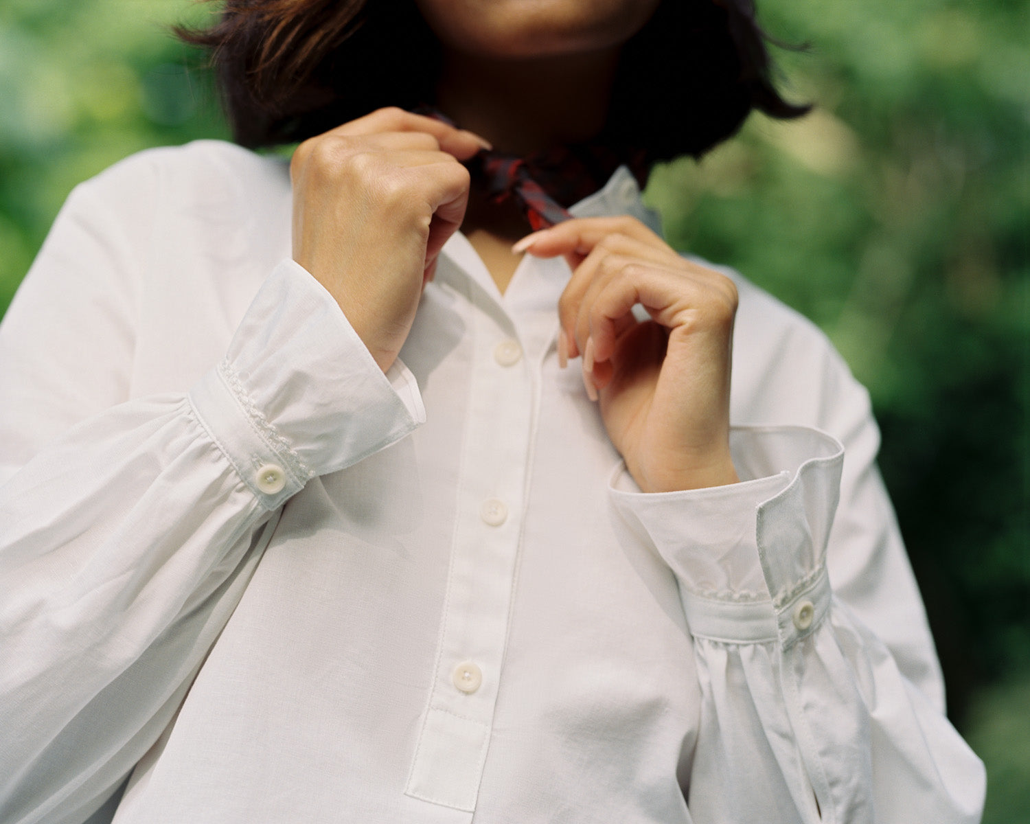 Recycled cotton white blouse - Saywood's Marie A-line blouse with gathered cuffs trimmed with lace. Model touches a red check neckerchief worn around her neck.