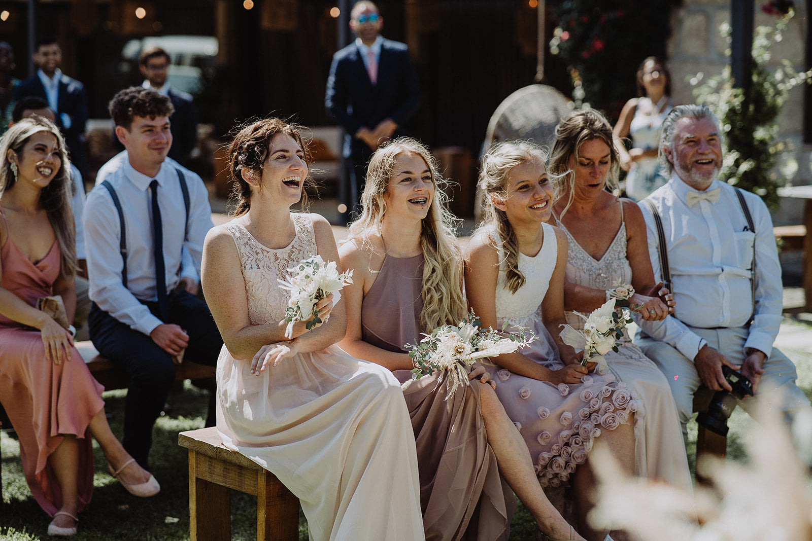 The Bridesmaids and Mother of the Bride seated at the outdoor ceremony, wearing their pre-loved dresses, laughing.