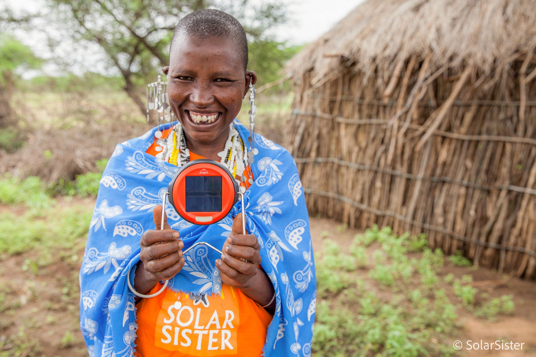 Solar Sister entrepreneur standing outside, smiling at the camera holding one of the products
