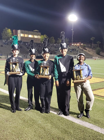 members of a high school band holding trophies on a football filed