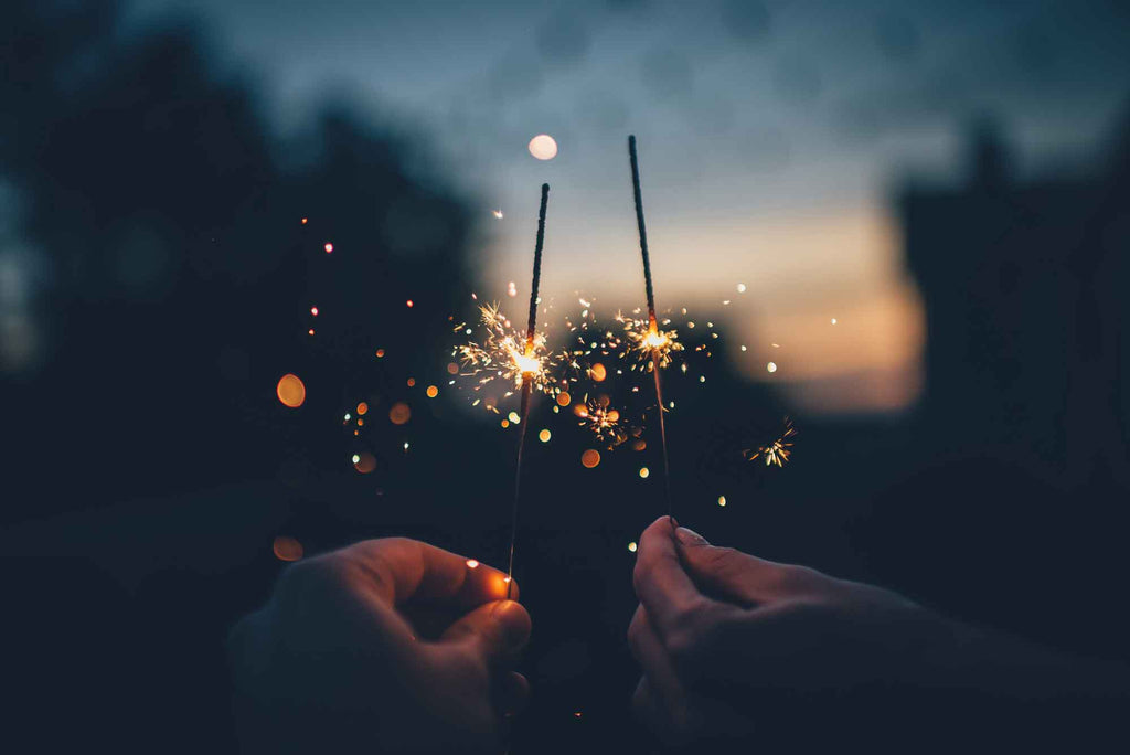 two hands holding sparklers close together at sunset