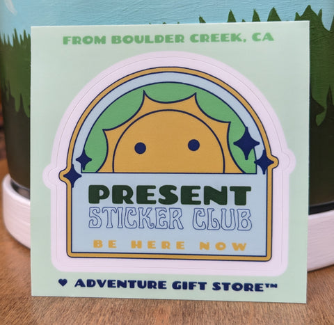 Present Sticker Club badge with sunshine and quote "Be Here Now"