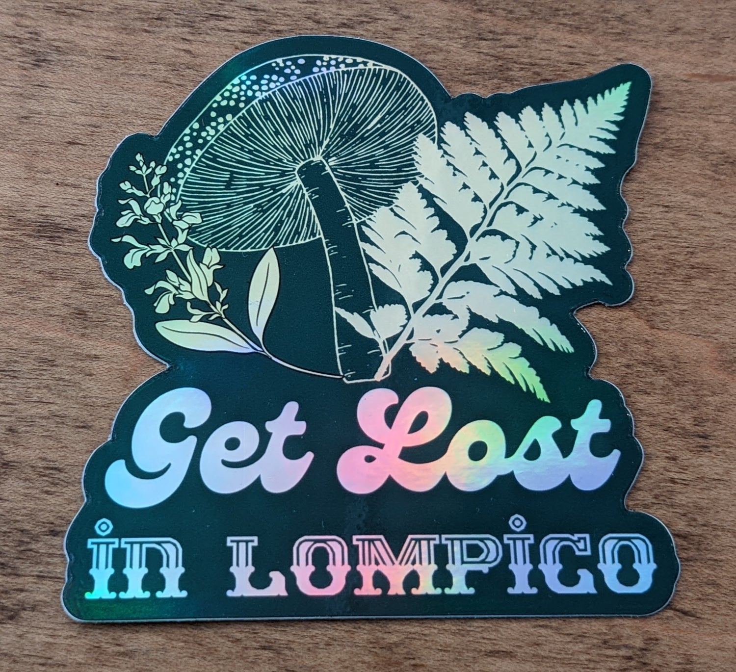 Mountain Talk holographic green sticker reading Get Lost in Lompico with fern and mushroom design