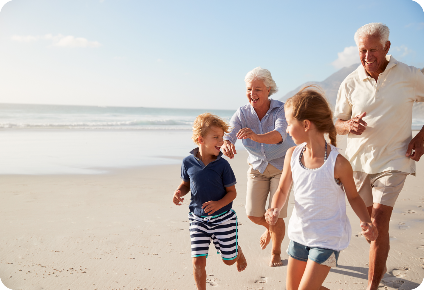 Photo of two grandparentd and two children running on the beach