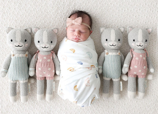 An image of a baby surrounded by Cuddle + Kind cuddly toys