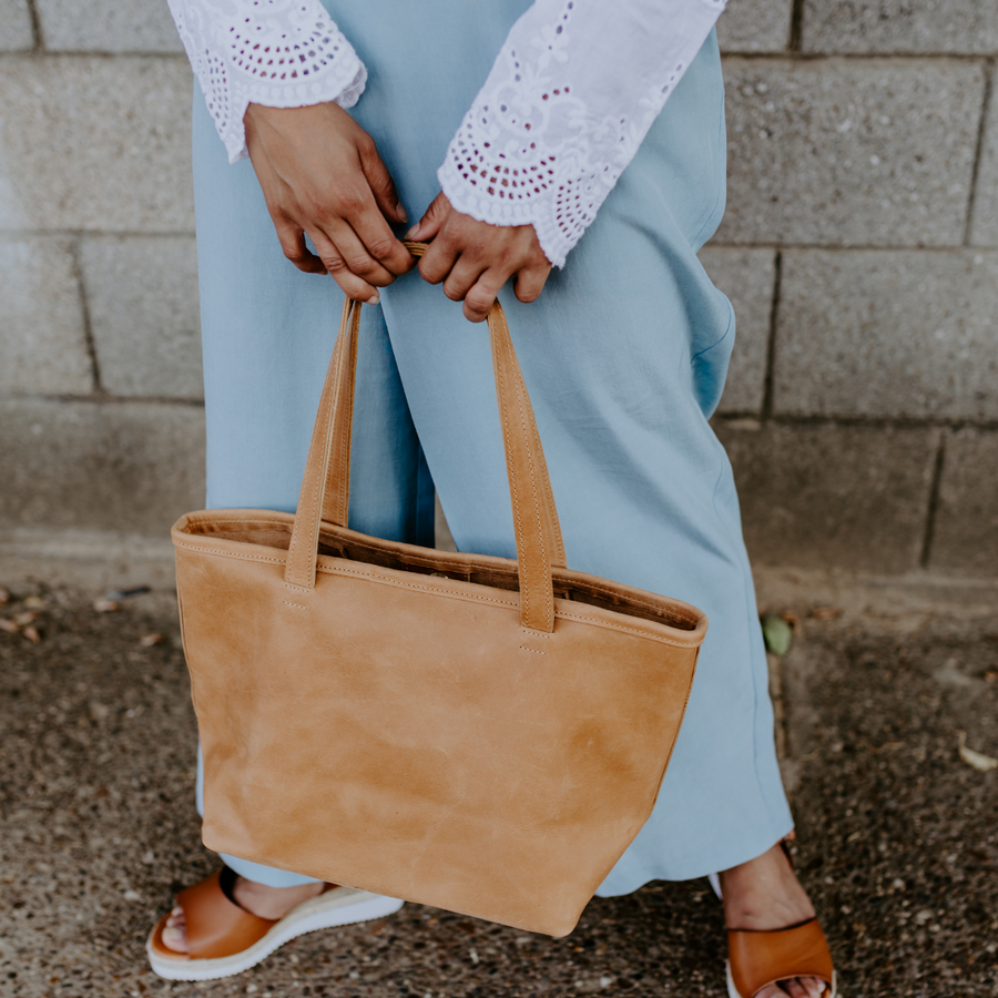 Woman carrying our Sand Amhara leather tote with comfortable shoulder straps that holds everything you need. Made of Ethiopian leather. Interior zippered pocket and interior snaps to change the look. Leather/metal key clasp. Flat bottom to sit easily.