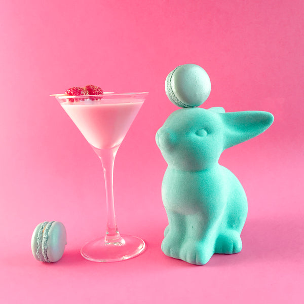 a green bunny on a pink background with green macarons and a pink cocktail 