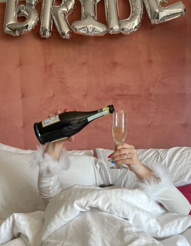 Bride pouring herself a glass of champaign in bed