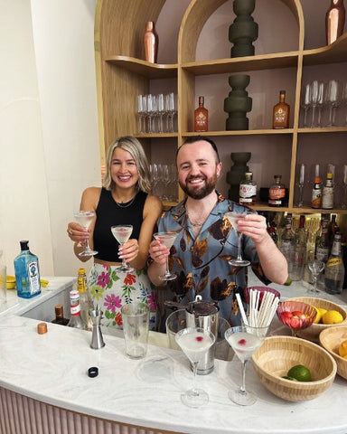 A couple holding up martinis behind the bar